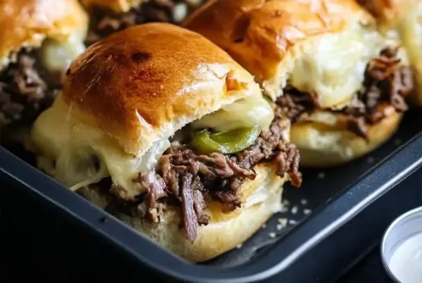 Close-up of a Philly Cheesesteak Slider with shredded beef, melted cheese, and green peppers, sandwiched in a glossy, golden-brown roll.