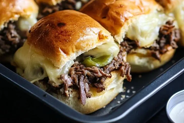 Close-up of a Philly Cheesesteak Slider with shredded beef, melted cheese, and green peppers, sandwiched in a glossy, golden-brown roll.