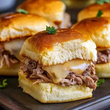 Close-up of a French Dip Slider made with tender shredded roast beef and melted Swiss cheese on a golden-brown Hawaiian roll, garnished with fresh parsley.