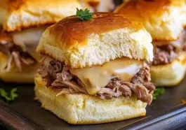 French Dip Slider with shredded roast beef and melted cheese on a toasted, golden slider bun, topped with parsley, served on a dark tray.