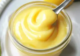 A jar of silky homemade lemon curd with a spoonful lifted, showing its thick, creamy texture and vibrant yellow color.