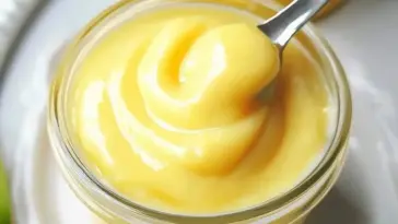 A jar of silky homemade lemon curd with a spoonful lifted, showing its thick, creamy texture and vibrant yellow color.