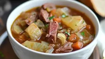 Close-up of a bowl of slow cooker corned beef and cabbage stew with tender beef, cabbage, carrots, and potatoes in a savory broth.