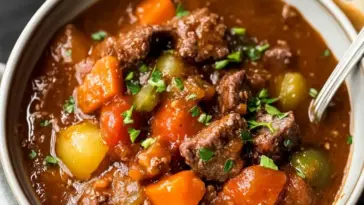 Bowl of homemade slow cooker beef stew with chunks of beef, carrots, potatoes, and celery in a thick brown sauce, garnished with parsley and served with a spoon.