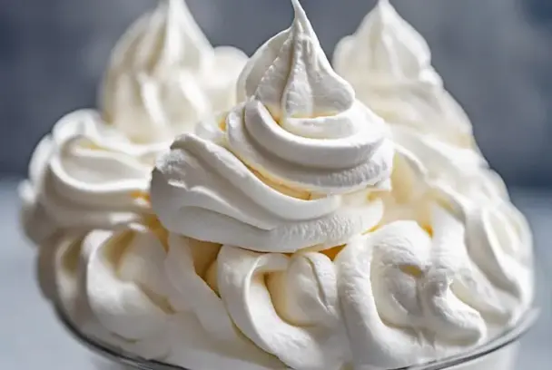 A swirl of stabilized whipped cream piped into tall, defined peaks in a glass bowl—smooth, airy, and perfect for cake decorating or dessert topping.