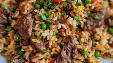 Close-up of homemade beef fried rice with tender sliced steak, peas, carrots, and green onions in a savory soy-based sauce.