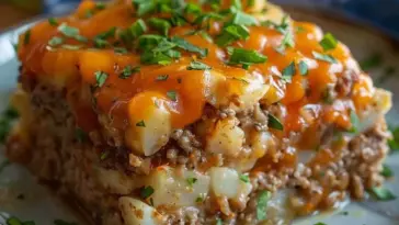 Close-up of Cowboy Meatloaf and Potato Casserole with layers of ground beef, diced potatoes, melted cheddar cheese, and fresh parsley on top.