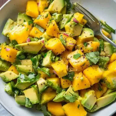 Bowl of fresh mango avocado salad with diced mangoes, avocado chunks, cilantro, and red onion, seasoned with lime and black pepper