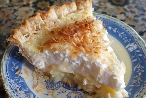 Slice of Old Fashioned Coconut Cream pie with whipped topping and toasted coconut on top.