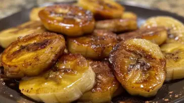 Close-up of pan fried cinnamon bananas, perfectly caramelized with golden edges and sprinkled with cinnamon, served on a dark plate.