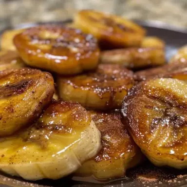 Golden brown cinnamon-sprinkled banana slices caramelized in a skillet and served on a dark plate, perfect for breakfast or dessert.