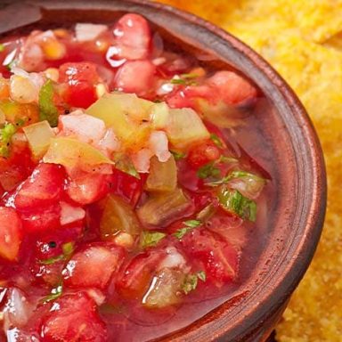 Close-up of fresh pico de gallo in a rustic bowl with diced tomatoes, onions, jalapeños, and cilantro, served with crispy tortilla chips on the side.