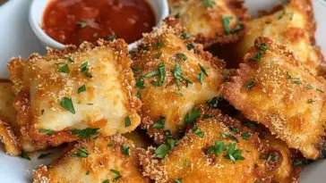 A plate of golden brown fried ravioli topped with fresh parsley, served with a side of rich marinara sauce in a small white bowl.