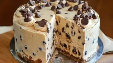 Close-up of a Chocolate Chip Cookie Dough Ice Cream Cake, showing thick layers packed with chocolate chips and cookie dough chunks, topped with whipped cream and chocolate pieces.