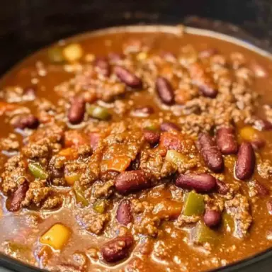 A slow cooker filled with hearty crockpot chili, featuring ground beef, kidney beans, bell peppers, and a rich tomato-based sauce, ready to be served.