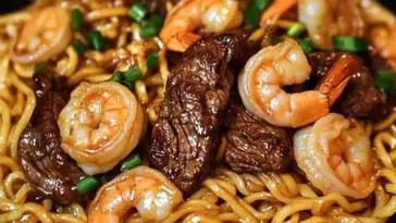 Plate of garlic butter steak and shrimp stir-fried noodles with tender beef slices, plump shrimp, and glossy noodles, garnished with green onions for a fresh touch.