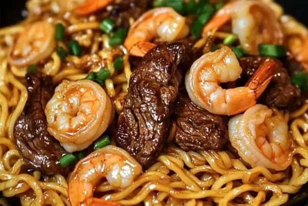 Plate of garlic butter steak and shrimp stir-fried noodles with tender beef slices, plump shrimp, and glossy noodles, garnished with green onions for a fresh touch.