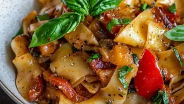 Bowl of Italian Drunken Noodles with wide egg noodles, sausage, vibrant bell peppers, and fresh basil, topped with cracked black pepper.