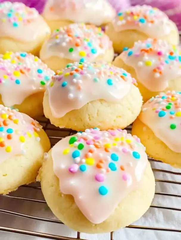 Soft Italian Easter Cookies shaped into knots and rings, topped with pastel-colored glaze and rainbow sprinkles, displayed on a spring-themed plate.