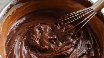 Close-up of smooth and glossy old fashioned fudge icing being whisked in a bowl, ready to frost cakes or brownies.