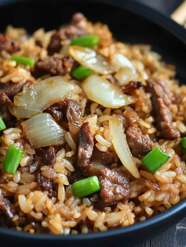 A skillet of onion beef fried rice with caramelized onions, sliced steak, and fluffy rice, garnished with green onions and sesame seeds – easy weeknight stir-fry.