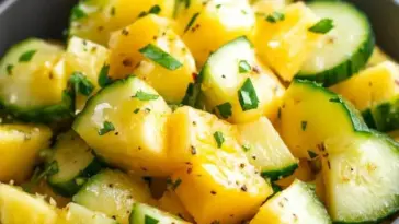 Bowl filled with bright pineapple chunks and sliced cucumber, tossed with fresh herbs and black pepper, creating a colorful and refreshing tropical salad.