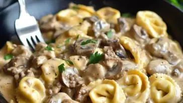 Skillet filled with creamy beef stroganoff tortellini, featuring golden cheese tortellini, savory beef, and mushrooms in a rich sour cream sauce.