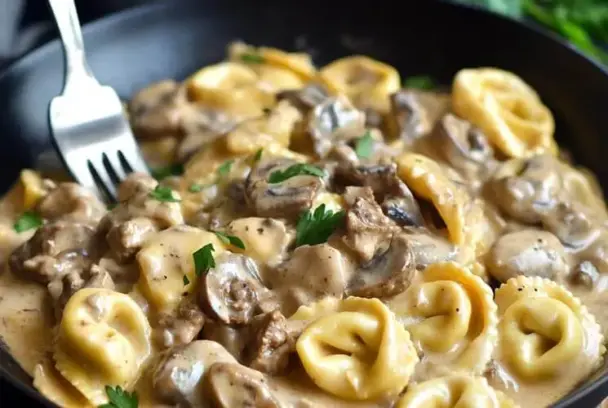 Skillet filled with creamy beef stroganoff tortellini, featuring golden cheese tortellini, savory beef, and mushrooms in a rich sour cream sauce.