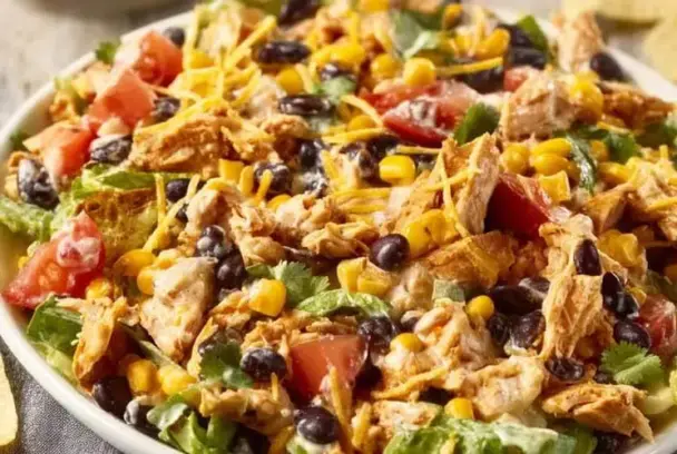 Vibrant chicken salad with shredded chicken, sweet corn, black beans, shredded cheese, chopped tomatoes, and cilantro over romaine lettuce.