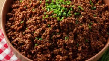 Close-up of seasoned ground beef in a bowl, topped with fresh chopped chives, set on a red and white checkered cloth — perfect for homemade Taco Bell tacos.