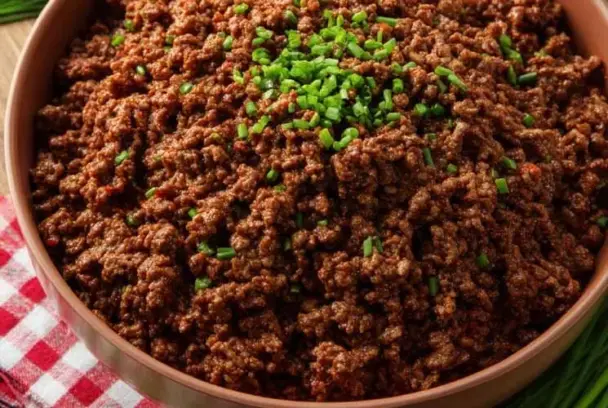 Close-up of seasoned ground beef in a bowl, topped with fresh chopped chives, set on a red and white checkered cloth — perfect for homemade Taco Bell tacos.
