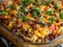 Baked Big Mac Casserole in a glass dish, featuring layers of seasoned ground beef, melted cheddar cheese, diced tomatoes, and fresh parsley on top.