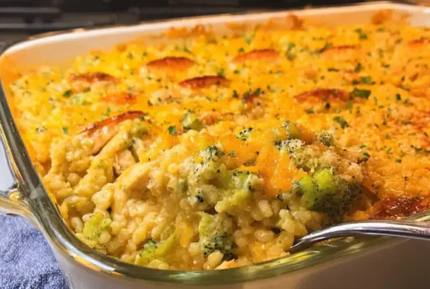 Freshly baked cheesy chicken broccoli rice casserole in a glass baking dish, topped with golden cheese and crispy browned spots, with a spoonful scooped out.