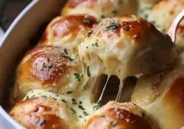 Golden brown cheesy dinner rolls in a baking dish, with one roll being pulled out showing stretchy melted cheese and parsley topping.