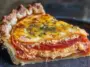 Close-up slice of cheesy tomato pie with layers of fresh tomatoes, creamy filling, and golden baked cheese in a flaky pie crust, served on a dark plate