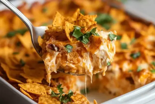 Cheesy Dorito Casserole being served from a white baking dish, showing melted cheese, crunchy nacho chips, and garnished with chopped parsley.