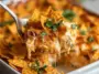 Cheesy Dorito Casserole being served from a white baking dish, showing melted cheese, crunchy nacho chips, and garnished with chopped parsley.