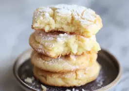 Close-up stack of gooey butter cake cookies dusted with powdered sugar, showing a soft, moist interior and slightly crisp edges.