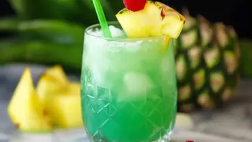 Bright green non-alcoholic tropical mocktail served in a patterned glass with ice, garnished with pineapple and a raspberry, with a green straw—ideal for Hawaiian-themed parties or summer drinks.