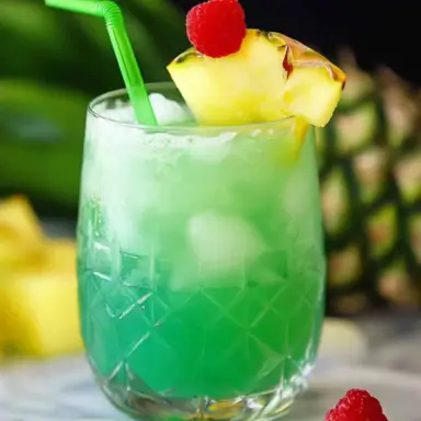 A vibrant green non-alcoholic Hawaiian mocktail served over ice in a crystal glass, garnished with a pineapple wedge and red raspberry, with a green straw—perfect for tropical summer parties.