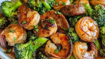 Glazed shrimp, caramelized sausage slices, and vibrant broccoli coated in a sticky honey garlic sauce, served in a white bowl.