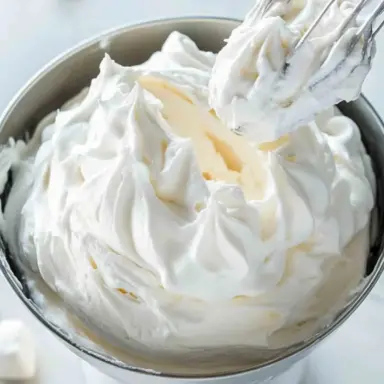 Whipped homemade marshmallow frosting in a metal mixing bowl with soft peaks, perfect for piping or toasting on desserts