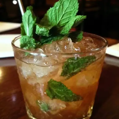 Close-up of a classic mint julep cocktail served in a lowball glass, filled with crushed ice and garnished with fresh mint leaves.