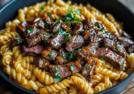 A bowl of one-pot smoky honey BBQ steak pasta with rotini noodles, tender sliced steak coated in a glossy BBQ sauce, and garnished with fresh chopped parsley.