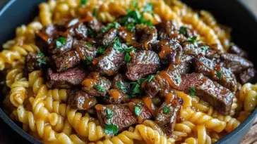 A bowl of one-pot smoky honey BBQ steak pasta with rotini noodles, tender sliced steak coated in a glossy BBQ sauce, and garnished with fresh chopped parsley.