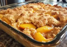Golden-baked peach dump cake with crumbly topping and sweet peach filling in a clear glass baking dish on a granite counter.