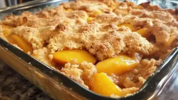 Golden-baked peach dump cake with crumbly topping and sweet peach filling in a clear glass baking dish on a granite counter.