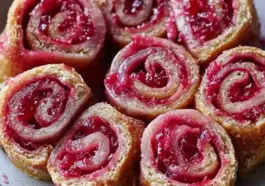 Golden brown rhubarb cranberry roll ups with a bright pink filling, arranged in a swirl pattern on a plate. A festive and easy fruit pastry perfect for brunch or dessert.