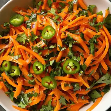 Bright shredded carrot and serrano chile salad in a white bowl, garnished with fresh cilantro and sliced green chilies — vibrant, spicy, and fresh.