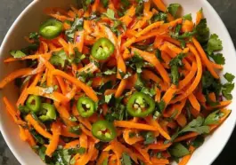 Top view of a vibrant shredded carrot and serrano chile salad with chopped cilantro, served in a white bowl — colorful, spicy, and fresh.